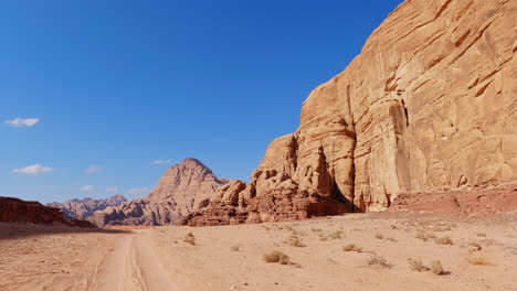 tall sandstone cliffs tower above sandy road track in the wadi rum desert