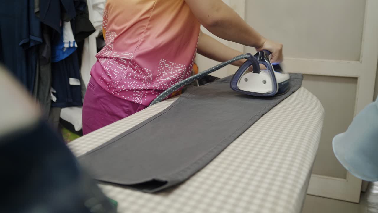 Closeup of a woman ironing clothing by stream iron on board at home
