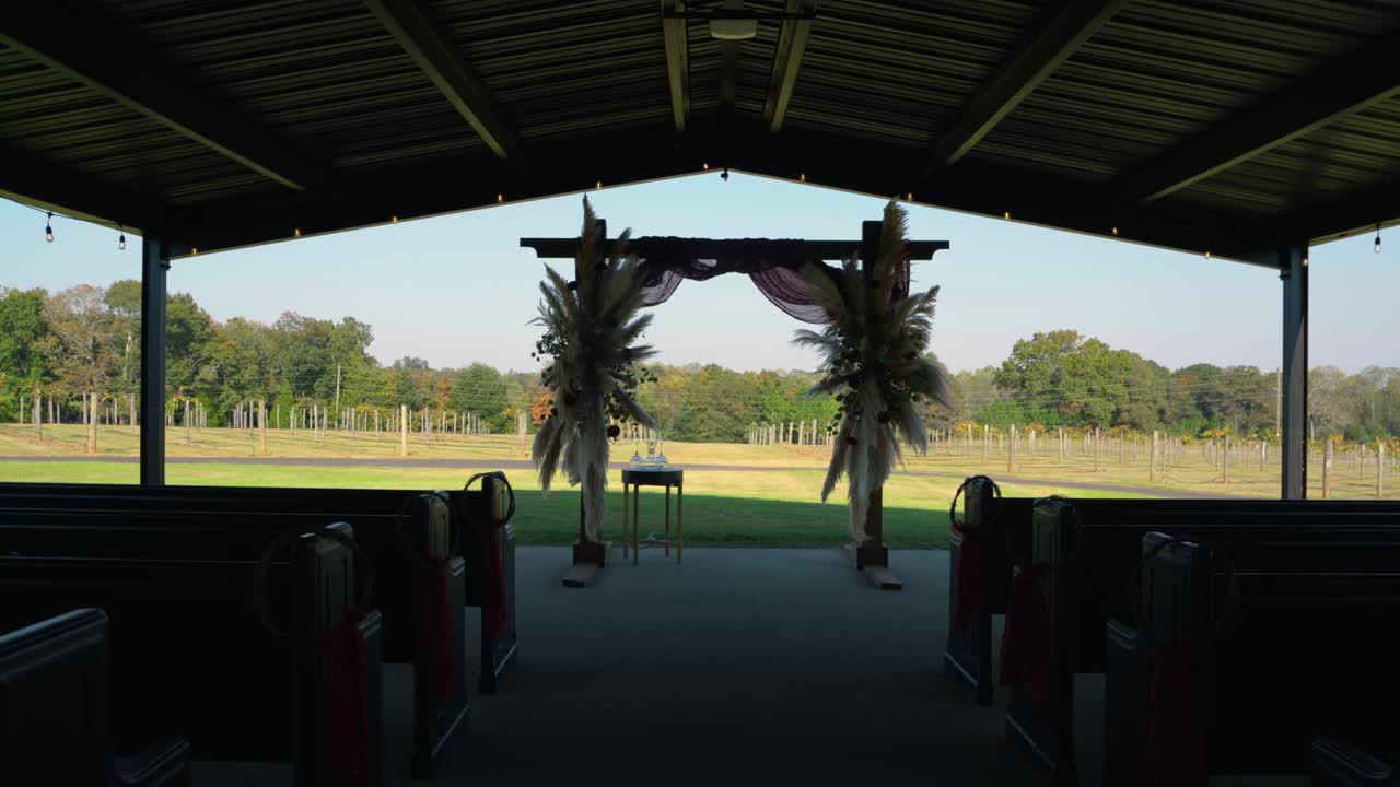 Wide shot of the wedding ceremony setup featuring rows of chairs leading to a beautifully adorned arch with pampas grass and florals, overlooking a vineyard in South Georgia.