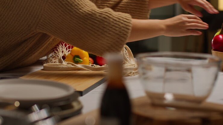 Primo piano di una donna che disfa una borsa di verdure fresche e salutari sul piano di lavoro in cucina.
