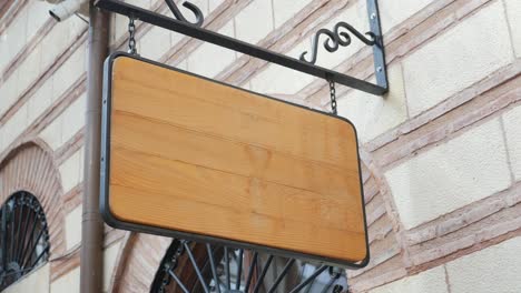 a blank wooden sign hanging on a brick wall.