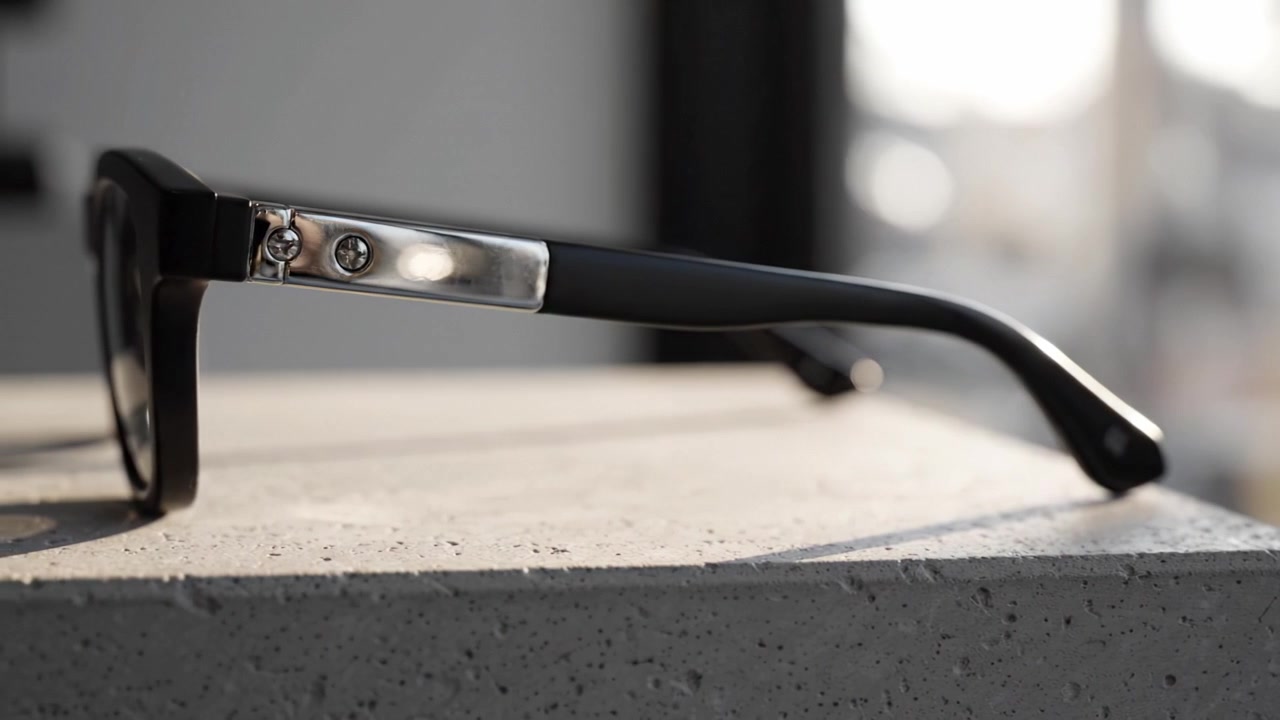 Primo piano di eleganti occhiali neri su una superficie di cemento, che mostrano un design unico e riflessi nella luce naturale, enfatizzando moda e funzionalità.