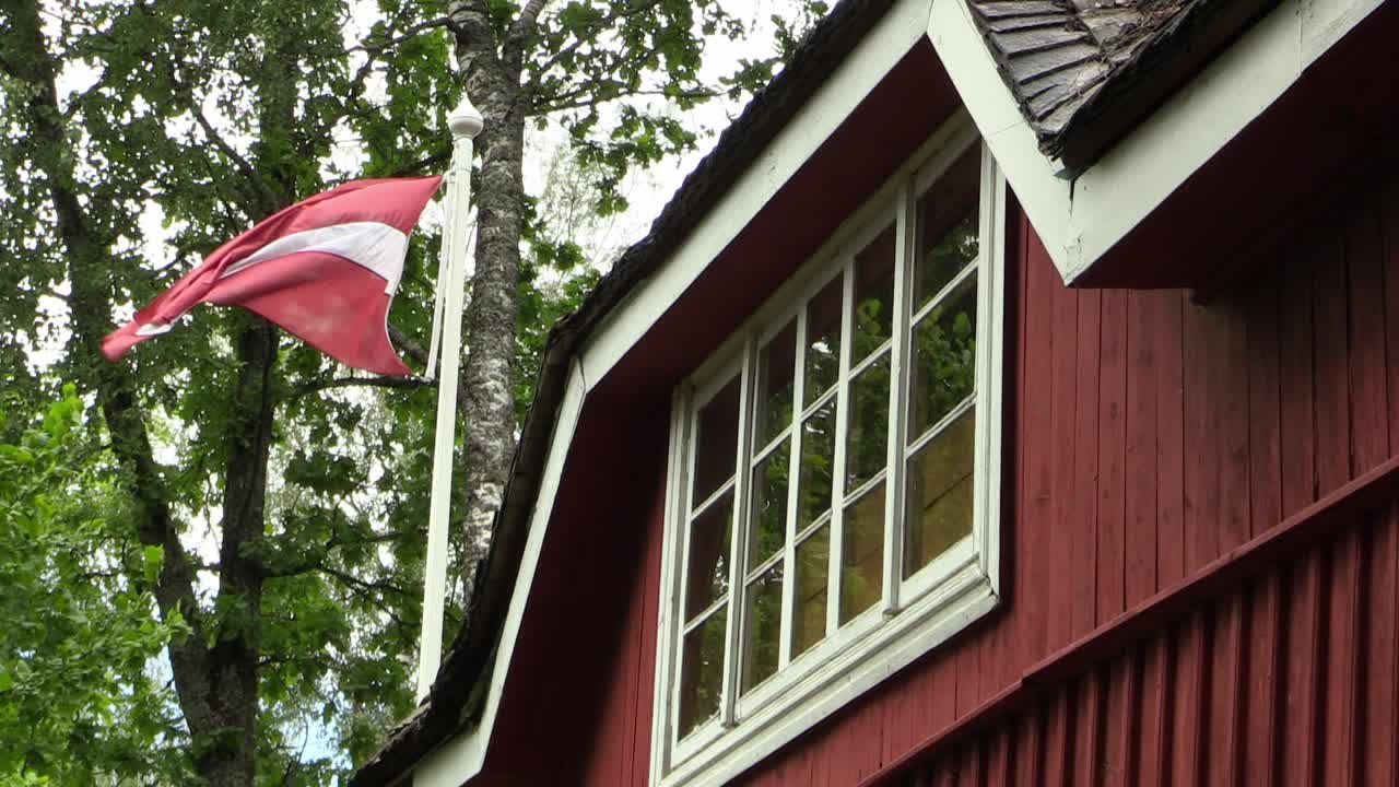 bandera letona ondeando junto a una antigua casa roja