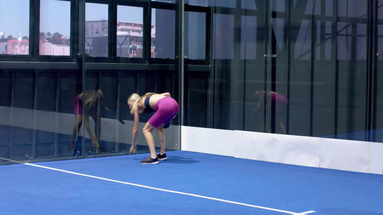 Woman playing padel tennis on indoor court, preparing to hit ball