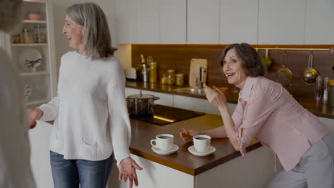 two older women hugging two older friends in the kitchen