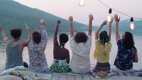 friends sitting on pier and dancing at lake party