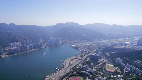 beautiful red running track and a green soccer field between the high-rise buildings and densely populated areas of sha tin hoi next to the main highways in hongkong