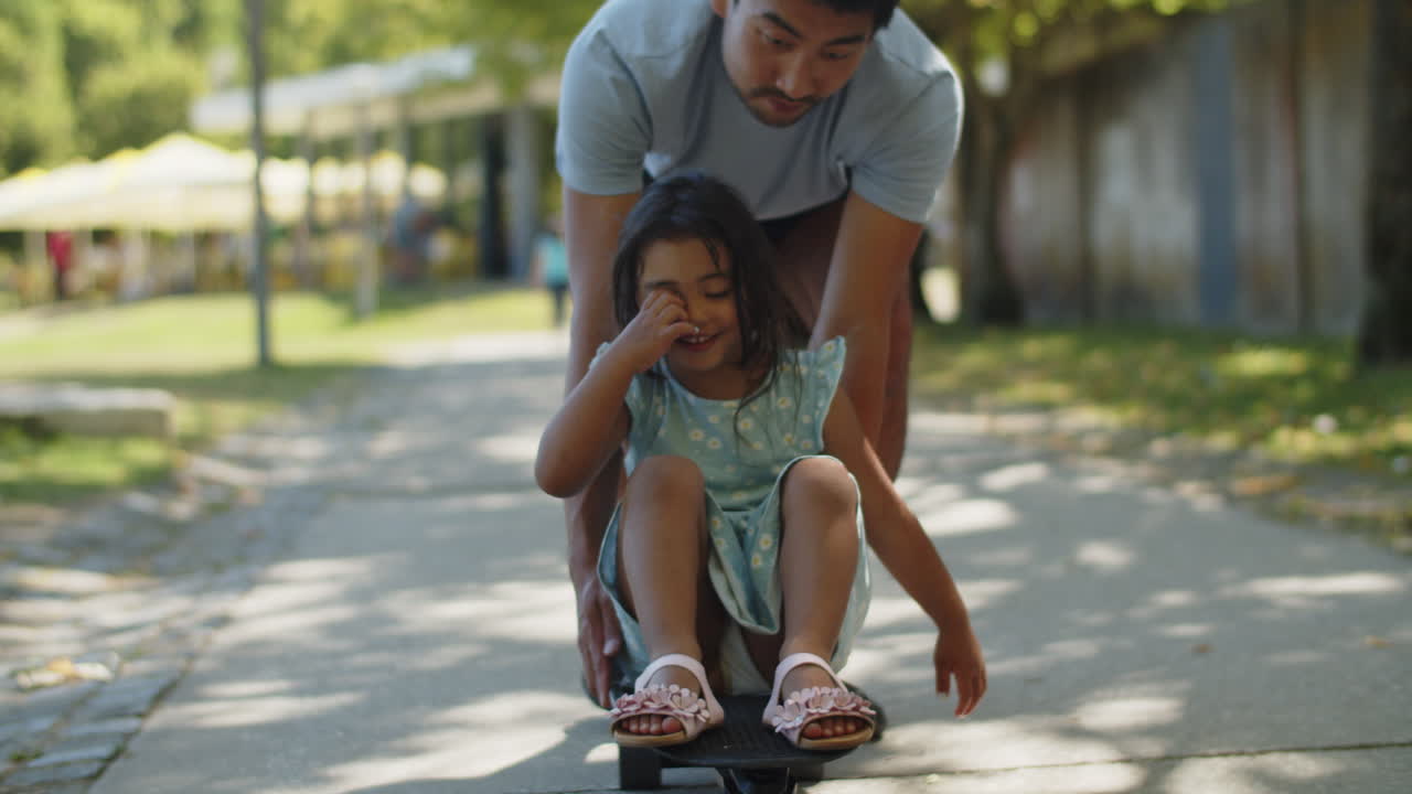 joven padre dando un paseo en patineta a su pequeña hija