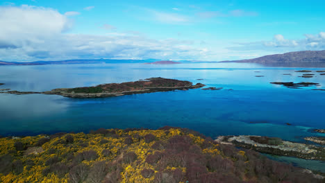 aerial trucking pan tilts up revealing vibrant yellow fields and deep blue waters off skye island scotland