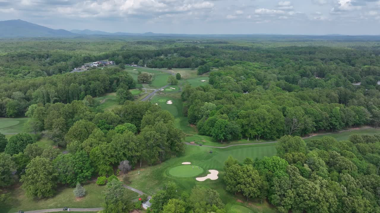 Gold course in american between green forest trees during cloudy day. Descend drone wide shot. Scenic suburb of Boonsboro Country Club in Lynchburg, Virginia.