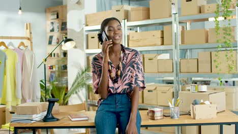 african american designer woman talking on the phone and leaning on the table in a fashion clothing store