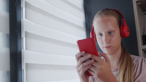 adolescente sentada junto a la ventana con un teléfono inteligente y auriculares