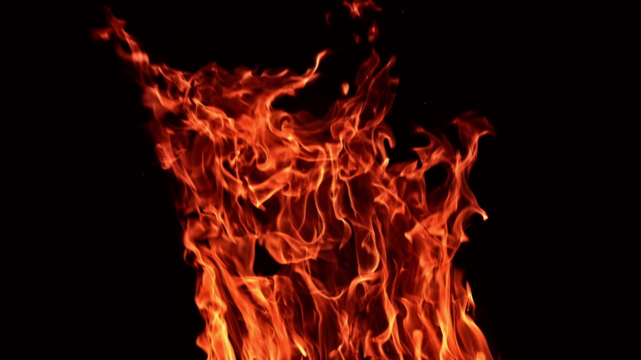 Large bonfire with flying flashes going up. Wooden sticks burn in the campfire at night.