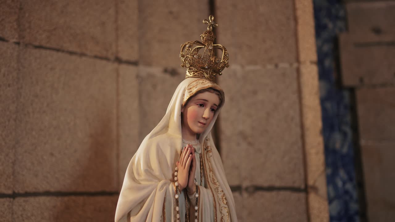 Statua incoronata della Madonna di Fatima in preghiera all'interno di una chiesa con mura in pietra.