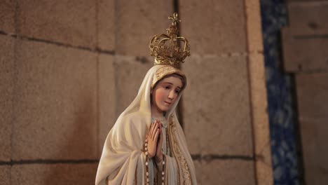 crowned statue of Our Lady of Fatima in prayer inside a stone walled church