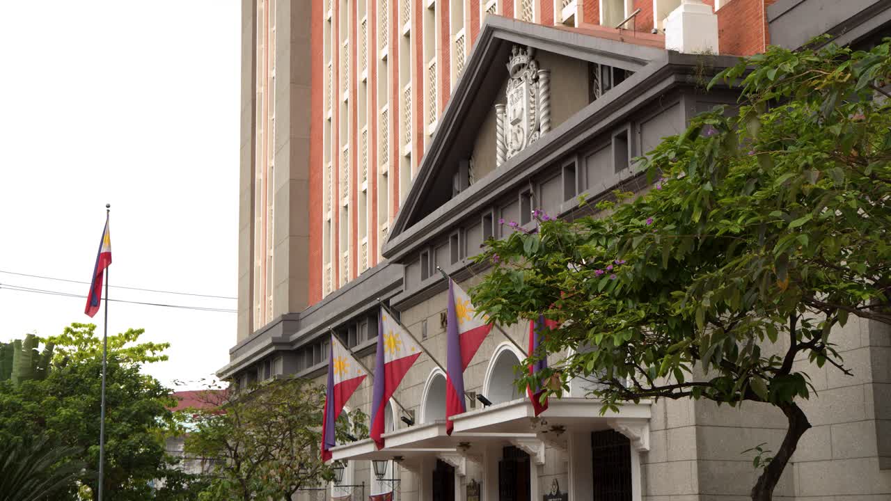 Inquadratura fissa dal basso di architettura coloniale e bandiere nazionali sotto la luce intensa del giorno a Manila.