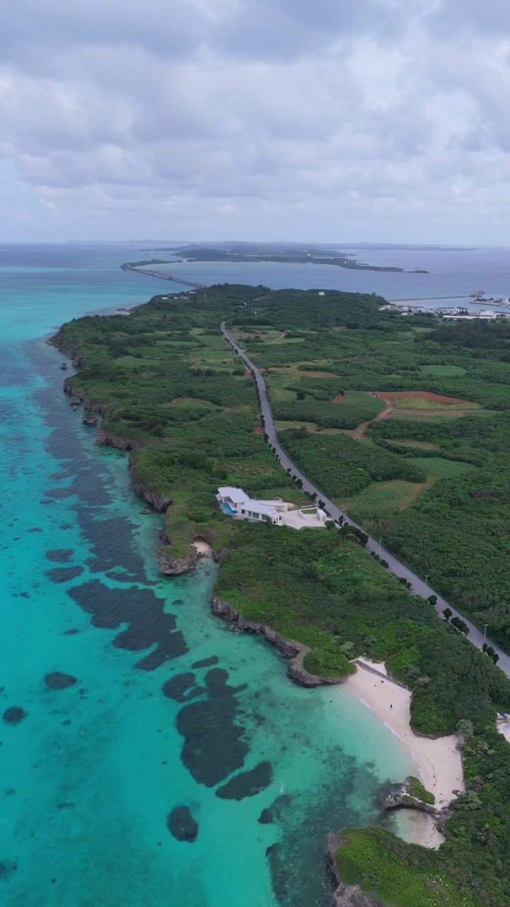 Vista aerea di una strada stretta tra alberi verdi con il ponte Ikema in lontananza in una giornata nuvolosa, Isola di Miyako, Okinawa, Giappone.