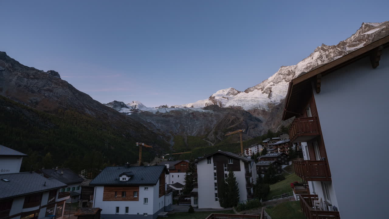 saas fee pueblo suizo glaciar glaciar pueblo suizo claro amanecer mañana cinematográfico lapso de tiempo grúas en movimiento zona de construcción picos de montaña iluminando con la primera luz aturdimiento