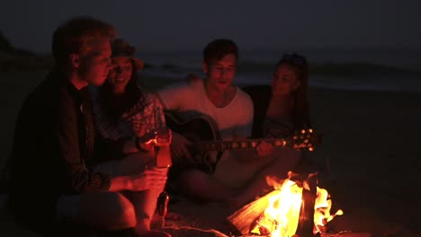 Picknick-Junger-Leute-Mit-Lagerfeuer-Am-Strand-Am-Abend.-Fröhliche-Freunde,-Die-Lieder-Singen-Und-Gitarre-Spielen.-Zeitlupe