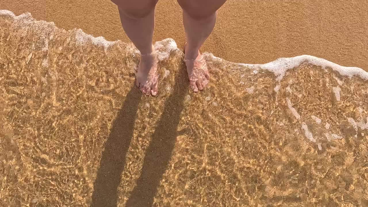 Bare feet on sandy beach with gentle waves in Phuket, Thailand. Warm lighting, calm atmosphere, and soothing water movement