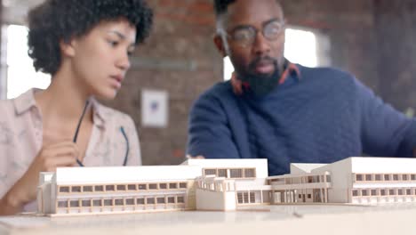 diversos colegas arquitectos enfocados discutiendo el trabajo con el modelo de construcción en la oficina en cámara lenta
