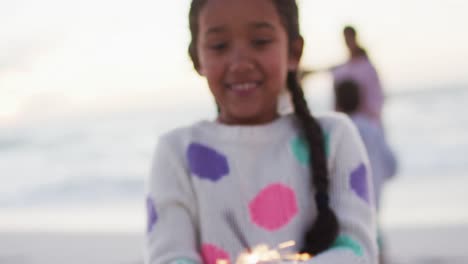 Porträt-Eines-Glücklichen-Hispanischen-Mädchens,-Das-Bei-Sonnenuntergang-Am-Strand-Mit-Wunderkerzen-Spielt