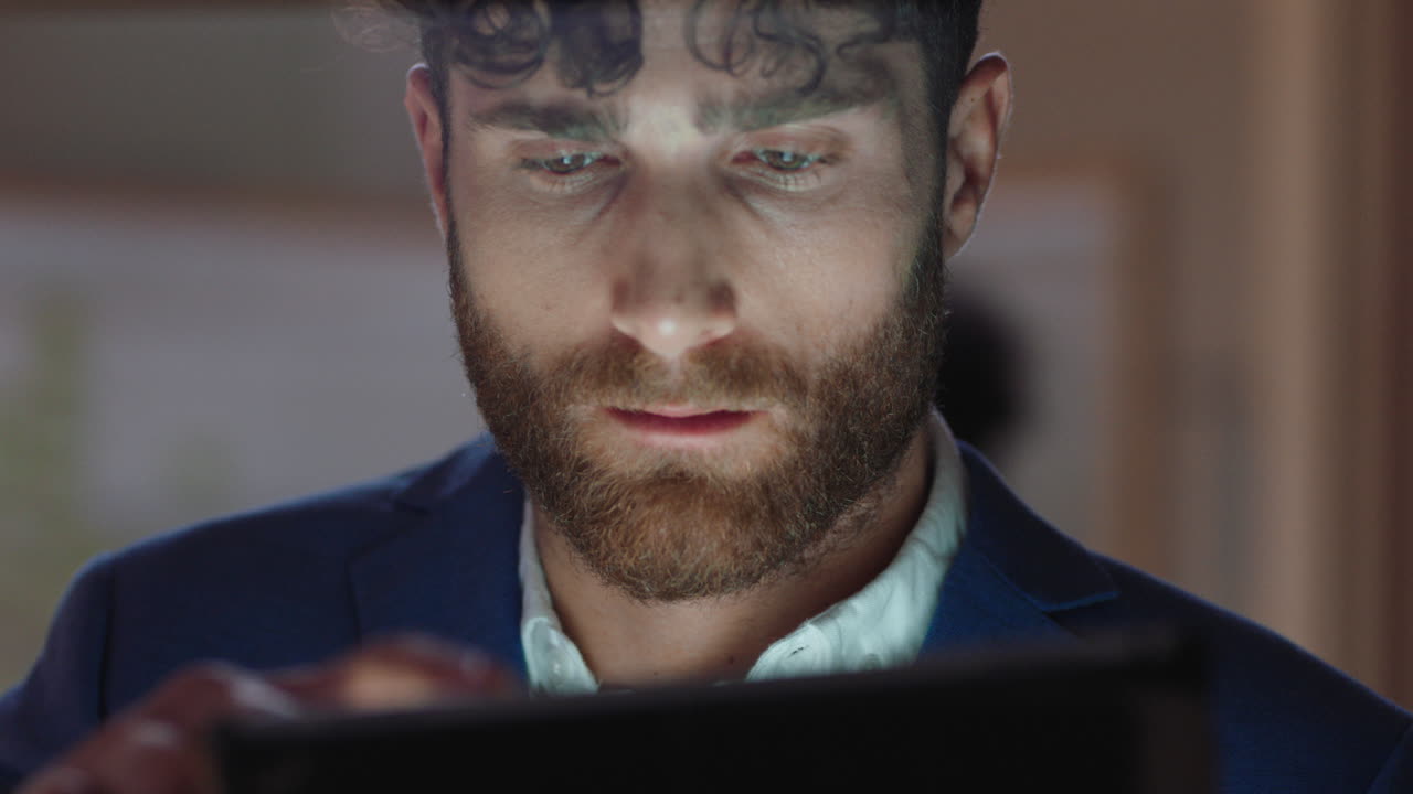 young businessman using tablet computer working late in office browsing information looking at data on digital touchscreen