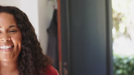 mitad de la cara de una feliz mujer biracial de pie y sonriendo en una casa soleada