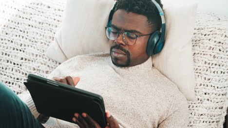 man relaxing on couch with headphones and tablet