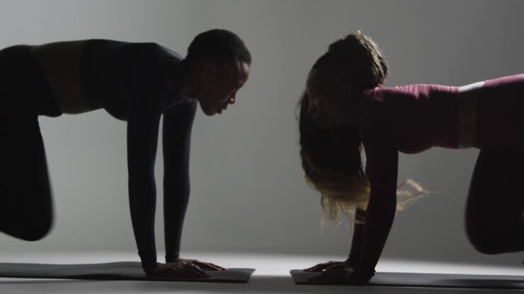 Studio Shot Of Two Women Wearing Gym Fitness Clothing Facing Each Other Exercising 4