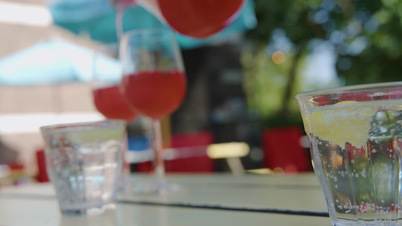 Lemon slice dropped into cocktail glass on sunny patio, colorful drinks, shallow depth of field