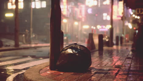 a lonely trash can sits on a wet, dark street corner in a city at night.