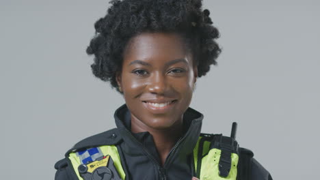 studio portrait of smiling young female police officer against plain background