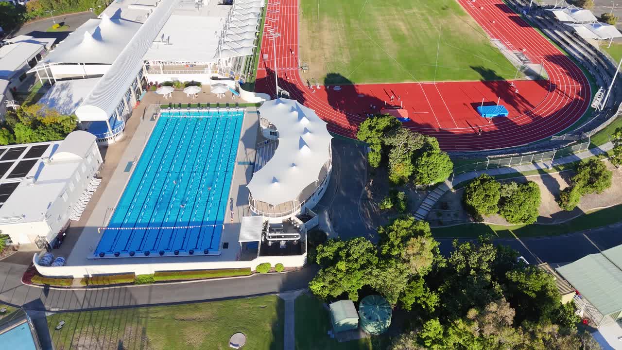 Drone captures vibrant sports facilities with pool, track, and fields in Gold Coast, Australia under bright daylight