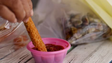 hand dips fried snack into spicy sauce