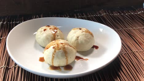 finishing plated steamed buns by adding black sesame seeds and green onions and soy sauce over buns