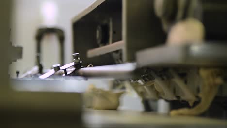 industrial machine cuts raw dough into even round balls traveling over conveyor belt inside bread factory