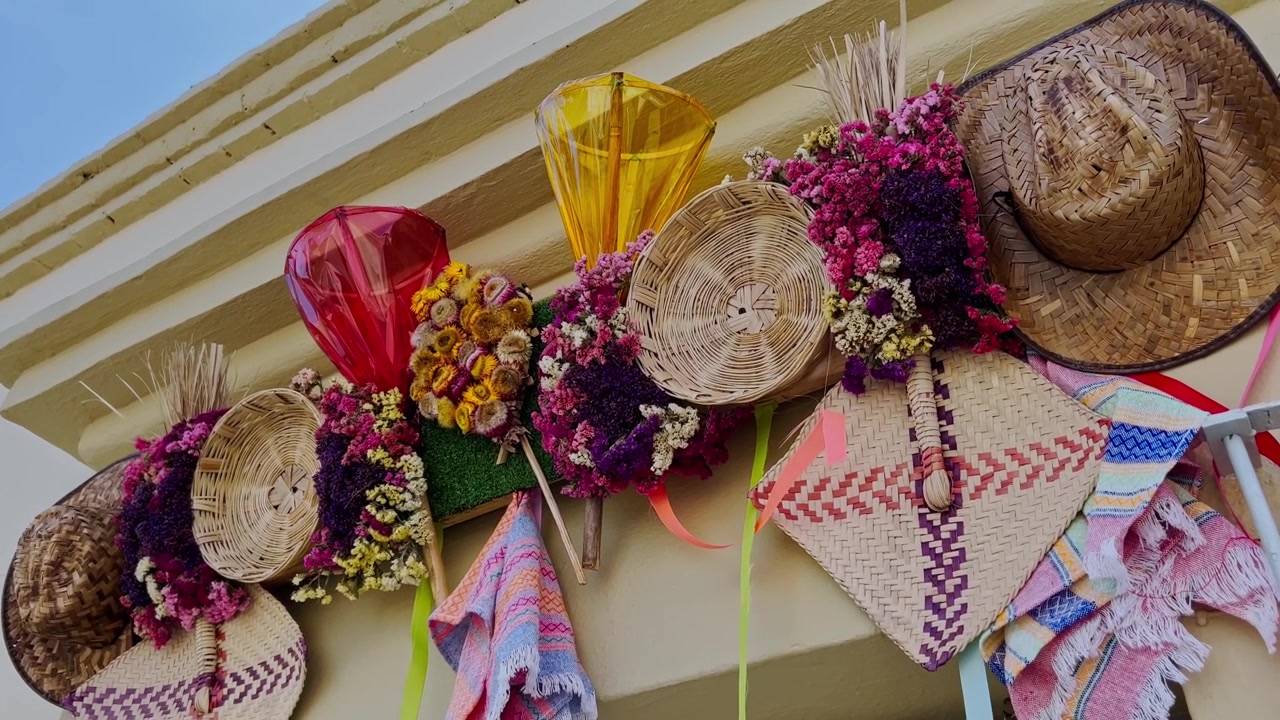 Inquadratura dal basso che mostra cappelli messicani colorati e decorazioni tradizionali esposti sulla facciata di un edificio bianco a Huatulco, Oaxaca, Messico, sotto la luce del giorno e un cielo azzurro.