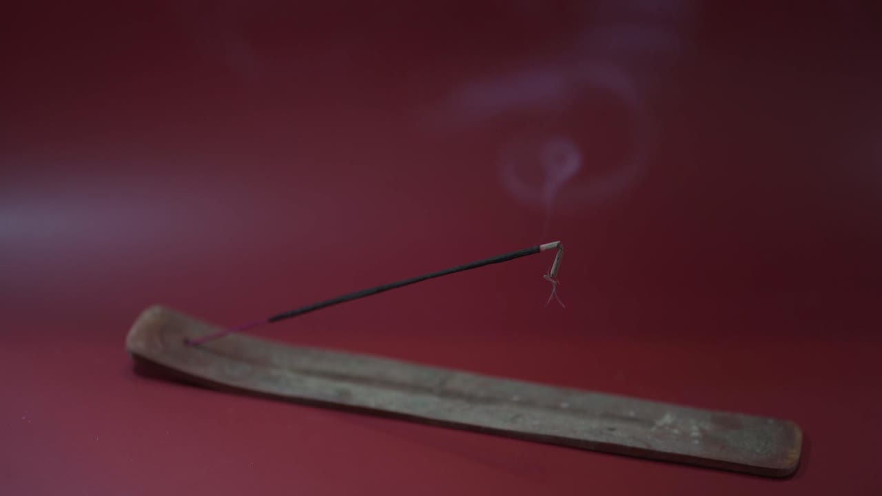 incense burns on an incense holder in front of a burgundy red background