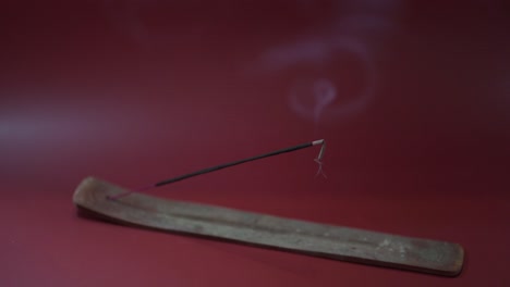 incense burns on an incense holder in front of a burgundy red background