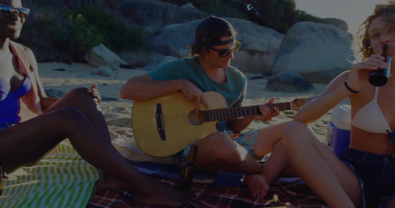Guitarist playing on beach, woman raising bottle while radial burst overlays trio for social toast