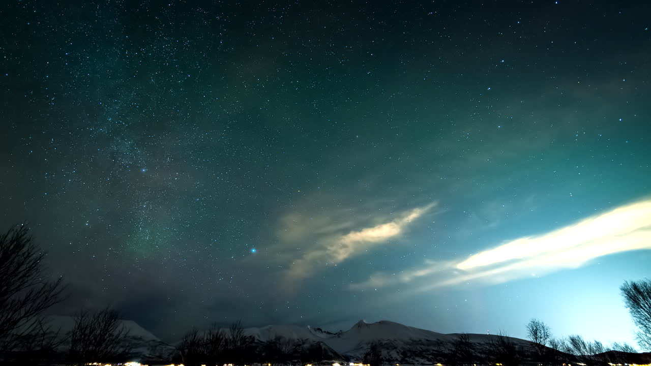 Night sky timelapse over Broskar in Norway, vibrant strand clouds reflecting light illuminating the winter landscape