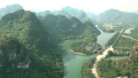 drone shot of a green river valley surrounded by limestone peaks, forest, and temple architecture—ideal for themes on eco-tourism, landscape, and southeast asian culture.