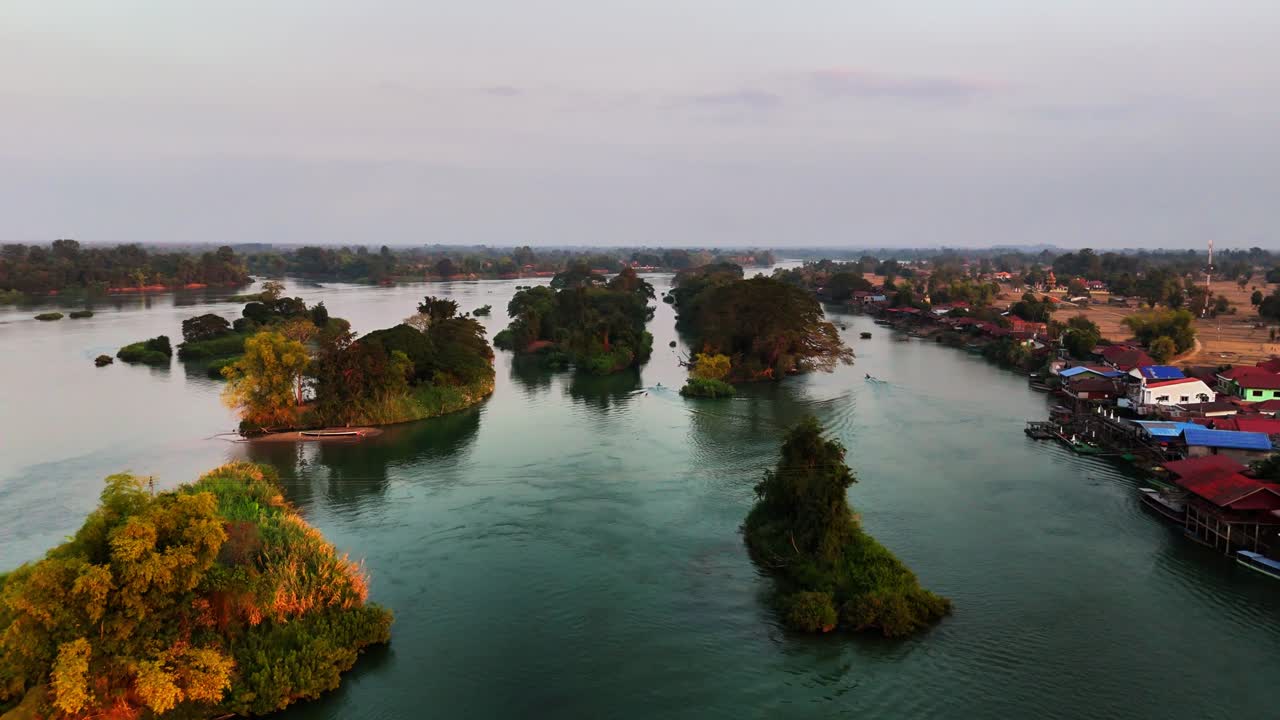 Lenta planata aerea sopra il tranquillo fiume Mekong vicino a Don Det, Laos, rivela isolotti coperti di alberi, case su palafitte lungo il fiume e terreni agricoli della stagione secca all'interno della regione di Si Phan Don all'ora d'oro