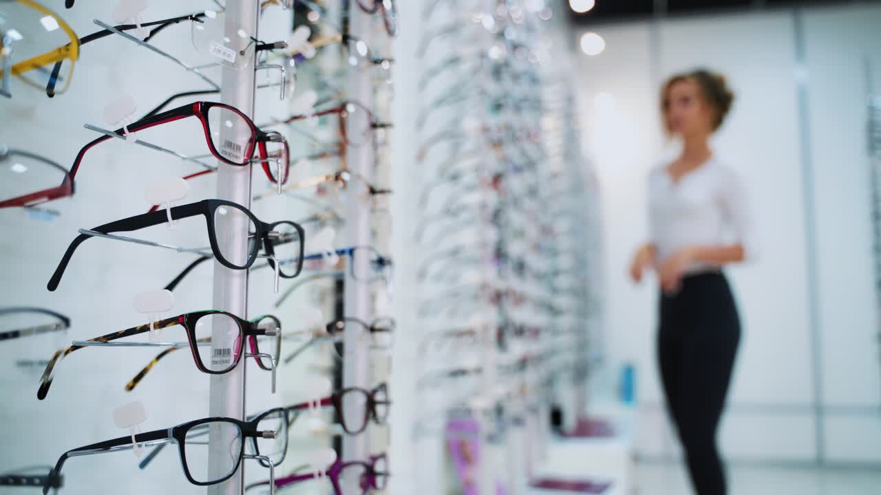 Eyeglasses concept. Fashionable glasses with colored frame on the stand in the optical store. Stylish eyeglasses on the blur background with customer.