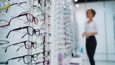 eyeglasses concept. fashionable glasses with colored frame on the stand in the optical store. stylish eyeglasses on the blur background with customer.