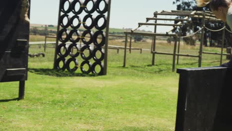 Fit-caucasian-female-soldier-exercising-on-obstacle-course,-climbing-over-fence-and-running