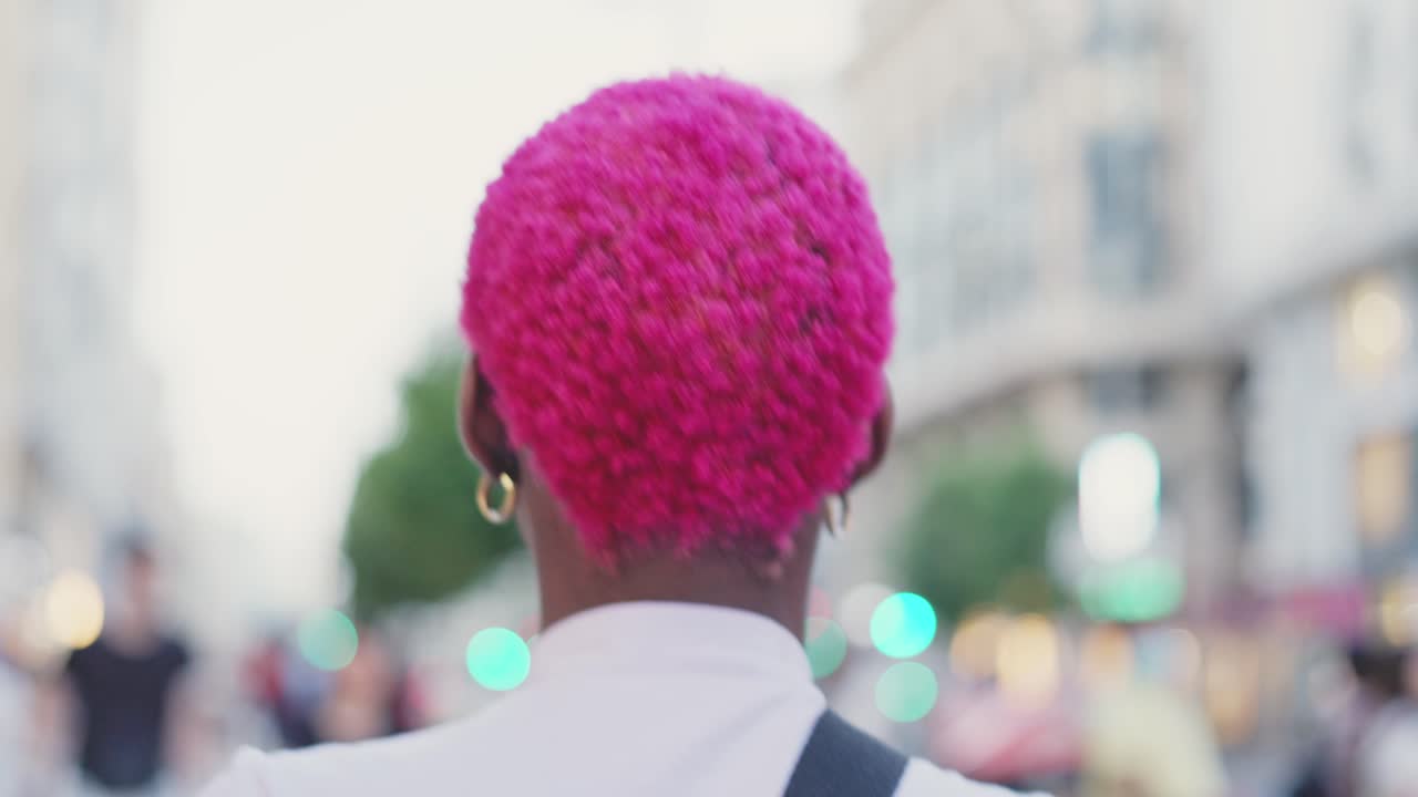 Person with vibrant pink curly hair walking in an urban setting