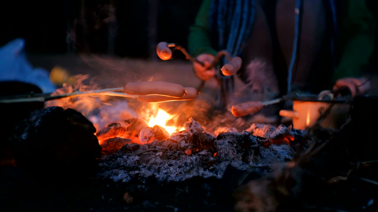 사람들은 밤에 숲에서 불에 소시지를 는다.