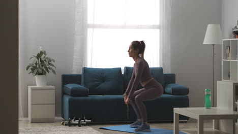 sporty woman dressed sportswear is doing squats with weight in hands training body keeping fit home fitness exercises full-length shot in apartment